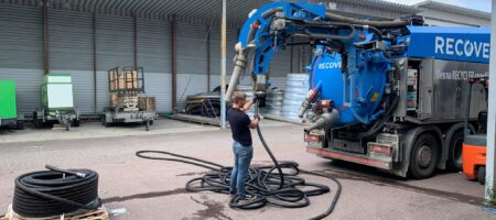 En man i svart t-shirt och jeans kopplar en slang till stort blått fordon