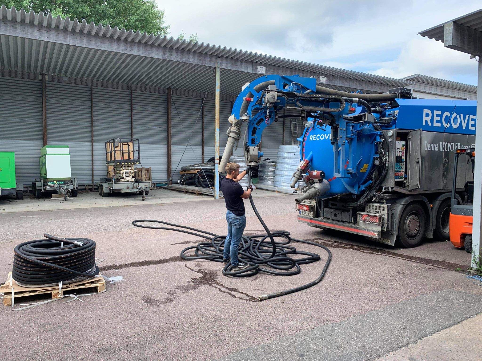 En man i svart t-shirt och jeans kopplar en slang till stort blått fordon