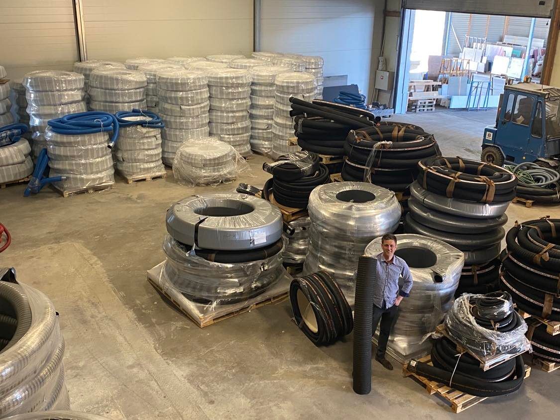 En man som står med inplastade svarta slangar på ett betonggolv i en lagerlokal.