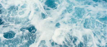 Närbild på klarblått hav och vågor som skummar.