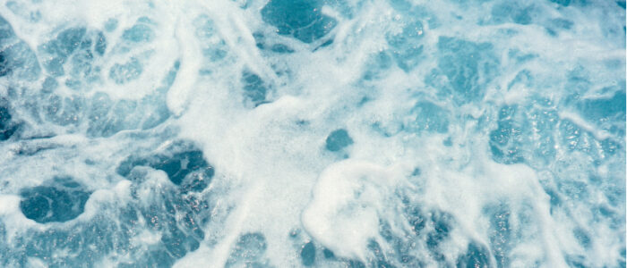 Närbild på klarblått hav och vågor som skummar.