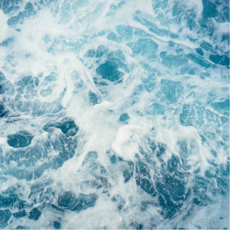 Närbild på klarblått hav och vågor som skummar.