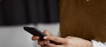 En kvinna som står med en mobil i handen.