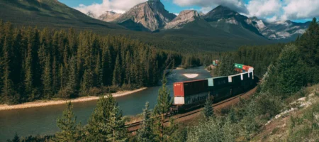 Tåg med containrar som åker bland skog och berg