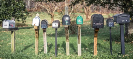 Flera brevlådor i olika färger och storlekar som står på träpinnar bredvid varandra.